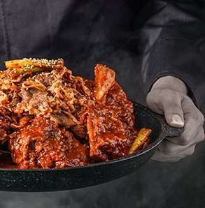 양념 고기를 담은 무쇠 팬을 든 손